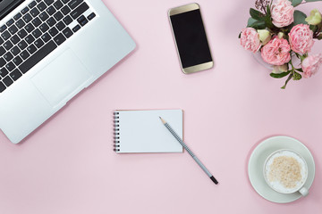 Top view of pink office desk table with laptop, smartphone, cup of coffee and flowers. Copy space, flat lay.