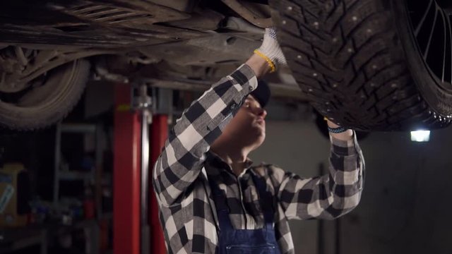 Handsome mechanic reparing a car fromthe bottom in his workshop.