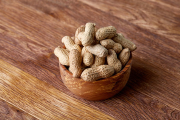 Unpeeled peanuts in wooden bowl over rustic wooden background closeup, selective focus
