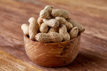 Unpeeled peanuts in wooden bowl over rustic wooden background closeup, selective focus