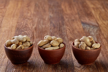 Three wooden bowls of unpeeled peanuts over rustic wooden background closeup, selective focus