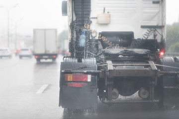 A truck moves along a rainy road, spray coming out from tires. view from the back of a lorry. No cargo trailer