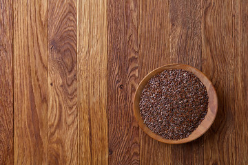 Flax seeds in a plate on wooden background, top view, close-up.