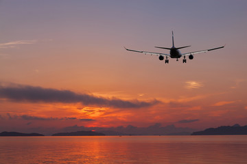 Fototapeta na wymiar Airplane flying over tropical sea at beautiful color sunset or sunrise scenery background.