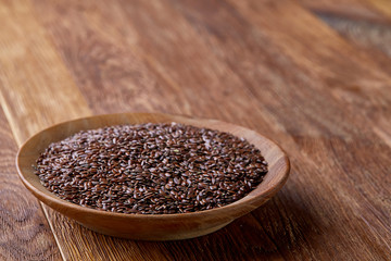 Flax seeds in a plate on wooden background, top view, close-up.