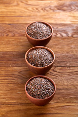 Three ceramic bowls with flaxseeds arrenged in row over wooden background, top view, selective focus