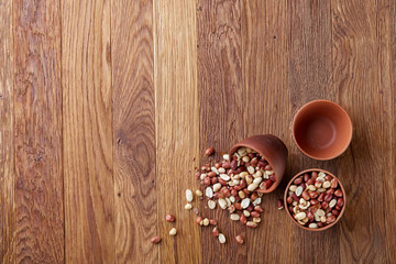 Two ceramic bowls with raw peanuts mix isolated over rustic wooden backround, top view, close-up.