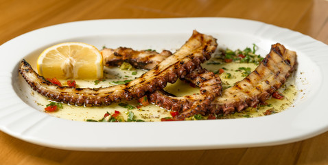 Grilled octopus tentacles with lemon and Greek spices. Top view. Wooden background. 