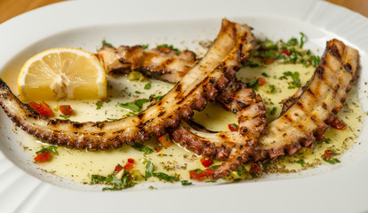 Grilled octopus tentacles with lemon and Greek spices. Top view. Wooden background. 