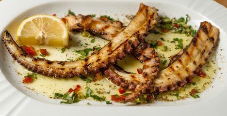 Grilled octopus tentacles with lemon and Greek spices. Top view. Wooden background. 