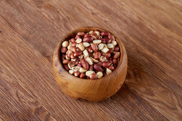 Raw mixed peanuts in wooden plate isolated over wooden background, top view, close-up.