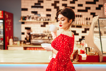 Glamour pin up girl drinks coffee in retro cafe
