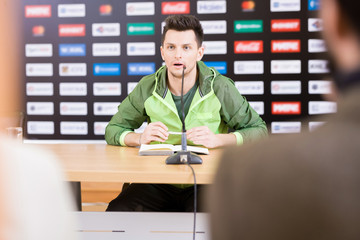 Waist-up portrait of handsome young soccer player looking at journalists and answering their...