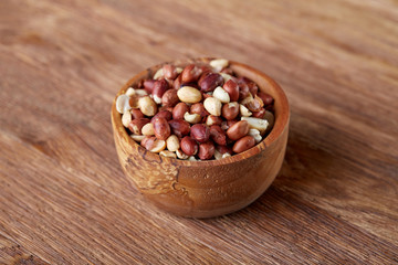 Raw mixed peanuts in wooden plate isolated over wooden background, top view, close-up.
