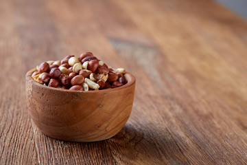 Raw mixed peanuts in wooden plate isolated over wooden background, top view, close-up.