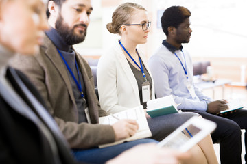 Obraz premium Group of journalists with notepads in hands sitting at spacious assembly hall while participating in press conference, blurred background