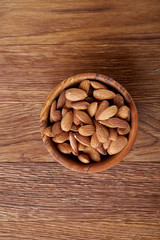 Ceramic bowl of almonds on wooden background, top view, close-up, selective focus.