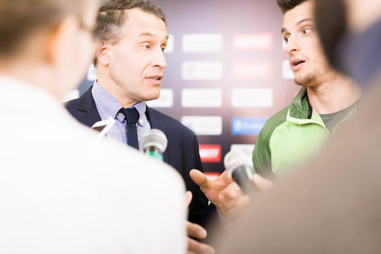 Over shoulder view of confident middle-aged head coach and talented young footballer answering questions of journalists after successful completion of match