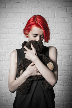Girl holding a toy. Soft toy-bear. Girl behind a brick wall.

