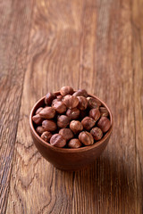 Hazelnuts in wooden bowl on wihite background with copy space, top view, selective focus.