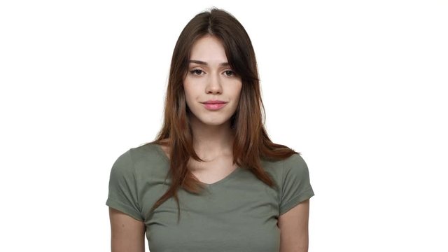 Portrait of gorgeous woman with long aubur hair wearing basic t-shirt posing at camera with kind smile, isolated over white background in studio. Concept of emotions