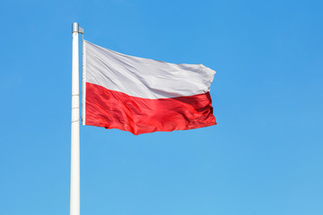 Fototapeta na wymiar Polish national flag waving on the wind against clear blue sky