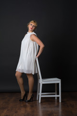 Young woman in white dress. Nearby is a white wooden chair. Shooting in the pavilion.
