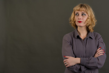 A woman with blond hair dressed in a gray shirt. Posing in the Studio on a gray background.
