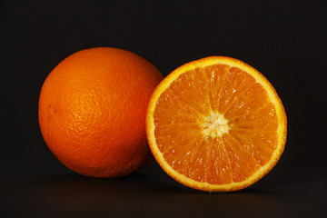 Orange, a whole orange, half orange, isolated on a black background. Front view. Copy space. Healthy nutrition, the concept of nutrition. A sweet ripe orange.