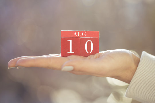 the woman is holding a red wooden calendar. Red wooden cube shape calendar for AUG 10 with hand 