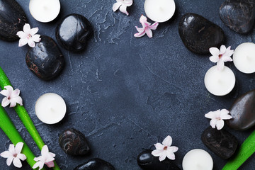 Spa background with massage pebble, green leaves, flowers and candles on black stone table top view. Aromatherapy, beauty, relaxation and zen like concept.