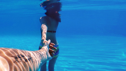 Follow me under the water. A woman is holding a man's hand. Hand with a tattoo. Underwater background