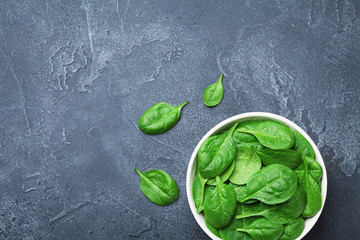 Green spinach leaves in bowl on black table from above. Organic food.