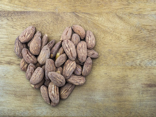 Roasted almonds on a wooden table, fruit are laid out in the shape of a heart. Copy space.