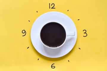 A cup of coffee on a yellow background (table) with watch face at 3 pm (3 am). Time to drink coffee