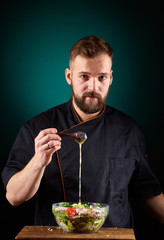 Portrait of a handsome male chef cook making tasty salad on a blurred aquamarine background