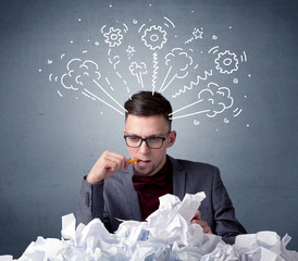 Young businessman sitting behind crumpled paper with drawings of gears and steam over his head