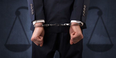 Arrested businessman in handcuffs with hands behind back and justice symbol wallpaper

