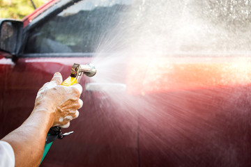 Man using water pressure washing red car. Automobile cleaning.