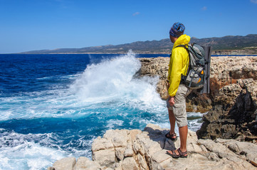 man with a backpack stands on a stone precipice and looks at a storm on the Mediterranean Sea