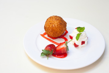 Fried ice cream with whipped cream and strawberry on plate.