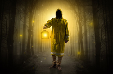 Man in raincoat coming from dark forest with glowing lantern in his hand concept
