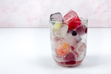 Berries frozen in ice cubes with mint in glass on wooden table background