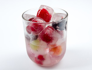 Berries frozen in ice cubes with mint in glass on wooden table background