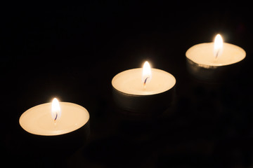 Three round burning candles on a black background.