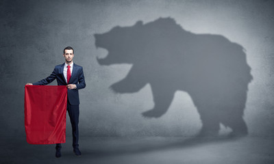 Businessman standing with red cloth in his hand and big bear shadow on his background
