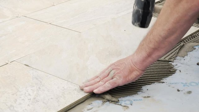 A man places a tile on the floor on top of cement. The tile is of mineral colors, like slate.
