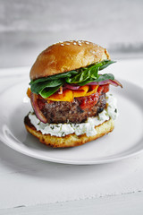 Burgers with grilled beef patties, cream cheese and spinach on classical bun. White wooden background