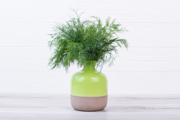 Bouquet of dill in ceramic vase. Bunch of dill in two-coloured ceramic pot on wooden background.