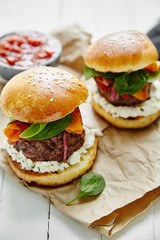Burgers with grilled beef patties, cream cheese and spinach on classical bun. White wooden background